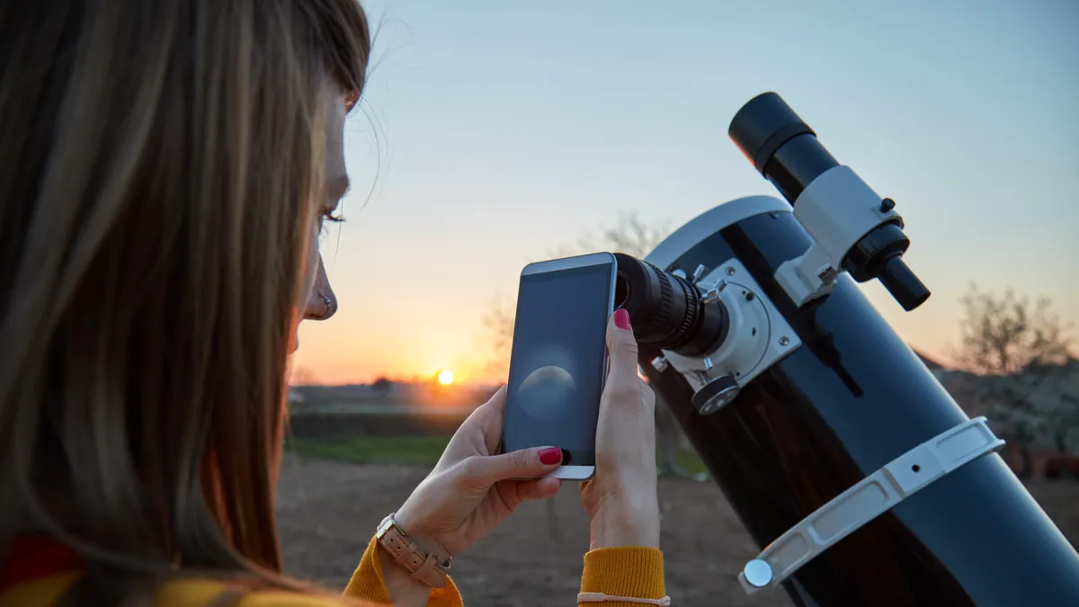 Person using a stargazing app on a smartphone under a clear, starry night sky with visible constellations and celestial objects.