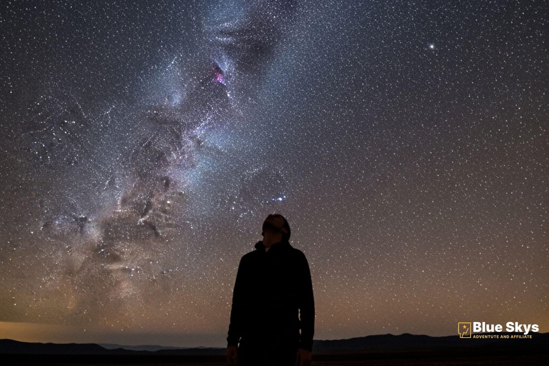 Person silhouetted against a breathtaking night sky with the Milky Way visible.